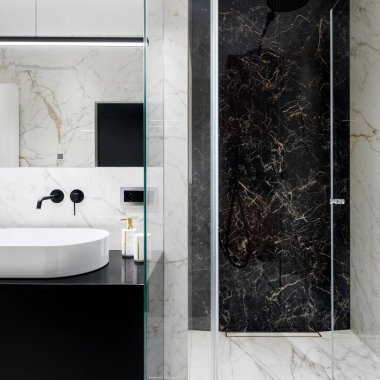 Duvarlarında ve zemininde siyah ve beyaz mermer döşemeleri ve siyah musluğu olan şık bir lavabosu olan zarif bir banyo.