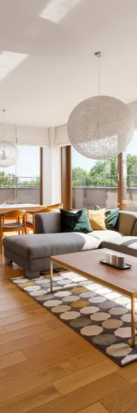 Vertical panorama of stylish living room with wooden floor, gray corner sofa and big ceiling cotton balls style chandelier