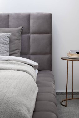 Rahat, yorgan kaplı, gri yatak başlığı ve zarif altından komodinli yatak çerçevesine yakın plan.
