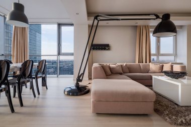 Lüks köşedeki kanepenin üstünde büyük, şık, siyah bir lamba. Pencere duvarı ve sandalyeli yemek masası olan zarif bir oturma odası.