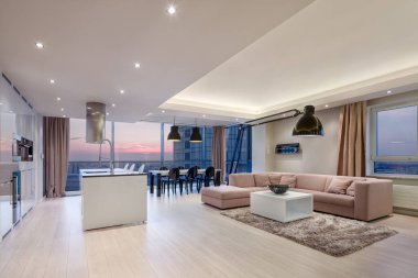 Şık oturma odası, mutfak ve yemek odası ve gün batımında büyük pencereleri olan lüks bir daire.