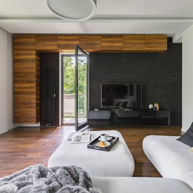 Siyah tuğladan duvarı, televizyonu, beyaz kanepesi ve balkon kapısı olan zarif bir oturma odası.