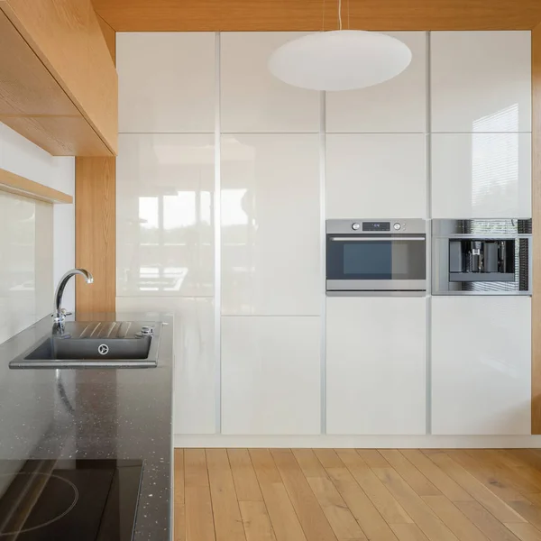 宽敞的厨房 有木制地板 长长的黑色台面和白色橱柜 墙上有咖啡机和烤箱 — 图库照片
