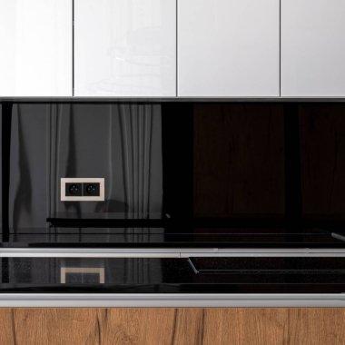 Siyah tezgahlı, arka kapaklı, beyaz ve ahşap dolaplı mutfak.