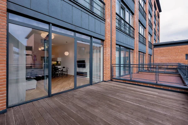 Elegant balcony with wooden floor in red brick building with big window open to modern apartment interior