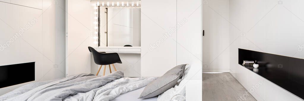 Panorama of elegant and white bedroom with dressing table with mirror and lights on hidden in wardrobe