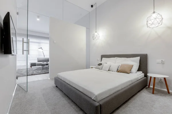 Big bed with gray frame in bright white bedroom with glass doors open to living room