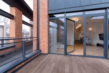 Ahşap zeminli, tuğladan duvarları olan büyük bir balkon ve pencere arkasında ışıkları olan modern bir çatı katı.
