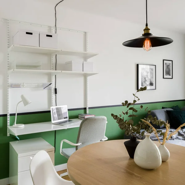 White industrial style home office area in living room with green wall and big wooden dining table