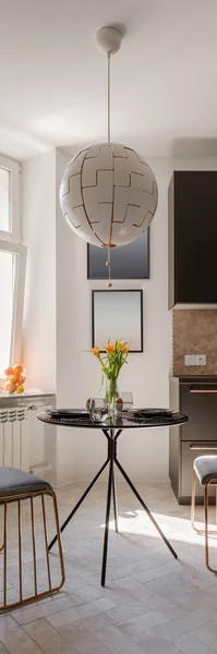 Vertical panorama of modern dining area with round, black dining table and two chairs under stylish pendant lamp