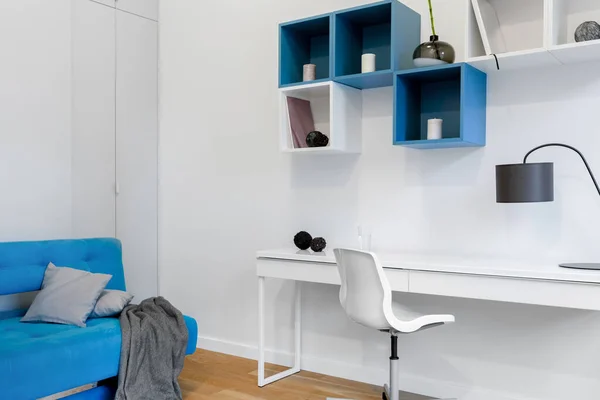 Simple and modern student room with white desk, blue couch and modern square shaped shelves