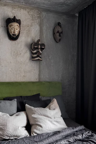 Dark and designed bedroom with industrial style wall and ceiling with exposed concrete and african masks