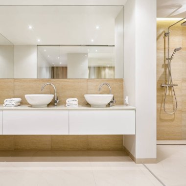 Zarif bir banyo, iki şık beyaz lavabo, büyük ayna ve duvarın arkasında duş.