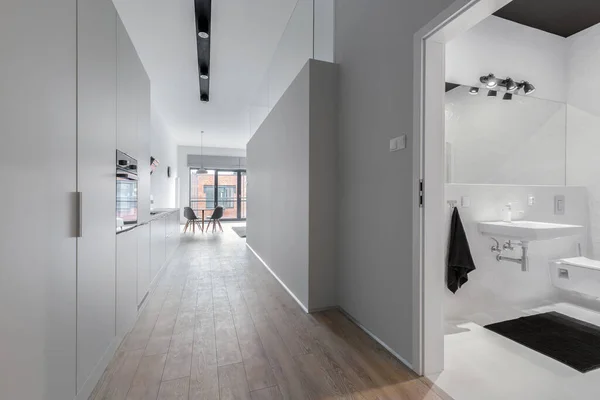 Gray and stylish corridor in apartment with gray walls and open doors to modern black and white bathroom interior