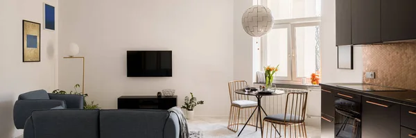设计精美的小公寓的全景 有雅致的客厅 时尚的餐桌 有新的金色椅子和现代黑色厨房在一个房间里 — 图库照片
