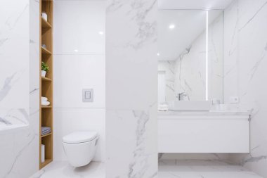 Lüks banyo beyaz mermer fayanslar, şık lavabo, tuvalet, büyük ayna, basit beyaz çekmece ve ahşap raflar