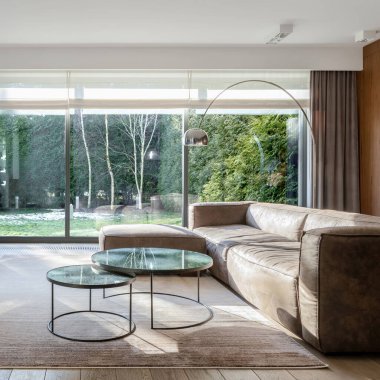 Lüks oturma odası, rahat kanepe, iki şık, yuvarlak sehpa ve bahçe manzaralı pencere duvarı.