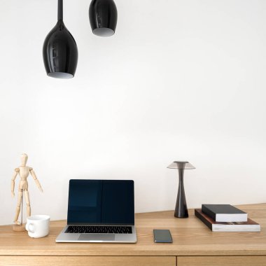 Bilgisayarı, kitapları, lambası ve süslemeleri olan küçük ahşap masa.