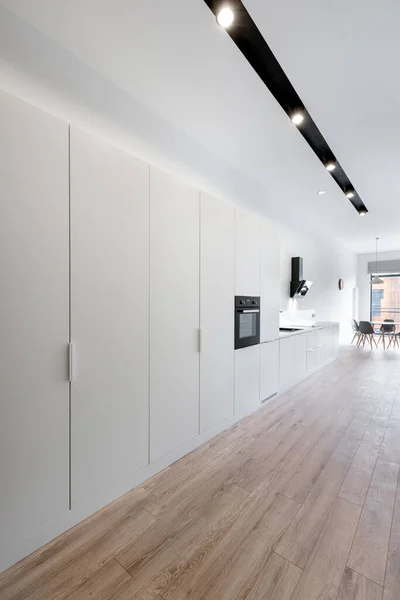 Long apartment corridor with wooden floor, white wardrobes and black ceiling lighting