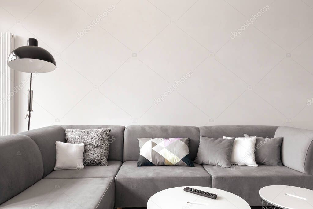 Big and comfortable gray corner sofa with decorative pillows and two white coffee tables