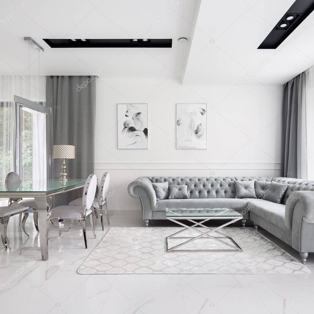 Glamour style living room with stylish, gray and quilted corner sofa with glass coffee table and big glass and silver dining table with elegant chairs