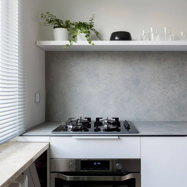 Simple style kitchen with gray countertop, white cupboards and kitchen hob with oven