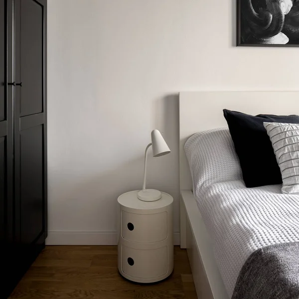 Black and white bedroom interior with big black wardrobe and simple white lamp on stylish white bedside table