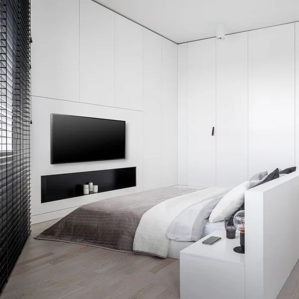Luxury white bedroom with big bed, many wardrobes and lockers, window with black blinds  and big television screen
