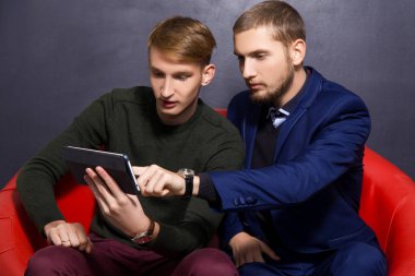 iki adam resmi tarzı ile bir tablet karanlık bir arka plan üzerinde kırmızı bir koltuk üzerinde oturuyor. İş kavramı