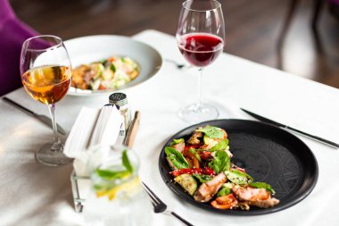 Orta kızarmış dana eti ve sebze, beyaz masa örtüsü, aletleri ve bir restoranda şarap ile bir tablo üzerinde siyah bir tabakta servis sıcak salata