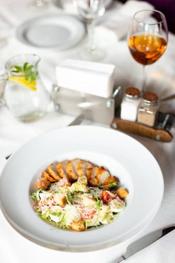 Romain salata Izgara tavuk, sarımsak croutons ve beyaz masa örtüsü, aletleri ve bir restoranda şarap ile bir tablo üzerinde beyaz bir tabakta servis parmesan ile