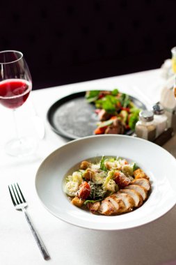 Romain salata Izgara tavuk, sarımsak croutons ve beyaz masa örtüsü, aletleri ve bir restoranda şarap ile bir tablo üzerinde beyaz bir tabakta servis parmesan ile