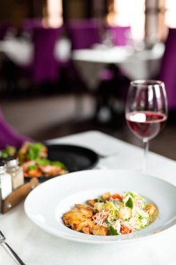 Romain salata Izgara tavuk, sarımsak croutons ve beyaz masa örtüsü, aletleri ve bir restoranda şarap ile bir tablo üzerinde beyaz bir tabakta servis parmesan ile