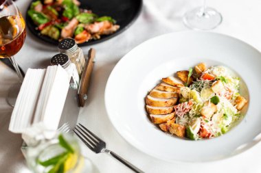 Romain salata Izgara tavuk, sarımsak croutons ve beyaz masa örtüsü, aletleri ve bir restoranda şarap ile bir tablo üzerinde beyaz bir tabakta servis parmesan ile