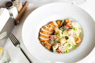 Romain salata Izgara tavuk, sarımsak croutons ve beyaz masa örtüsü, aletleri ve bir restoranda şarap ile bir tablo üzerinde beyaz bir tabakta servis parmesan ile