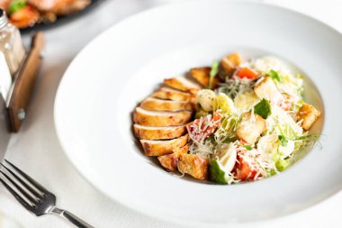 Romain salata Izgara tavuk, sarımsak croutons ve beyaz masa örtüsü, aletleri ve bir restoranda şarap ile bir tablo üzerinde beyaz bir tabakta servis parmesan ile