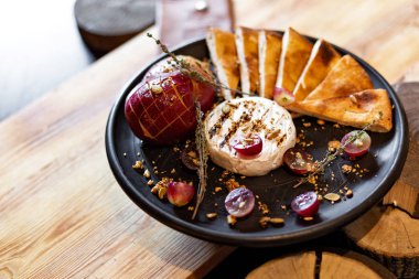 Izgara peyniri ile pişmiş elma ve üzüm ile dilim ekmek, rustik tarzı ahşap arka plan üzerinde siyah bir tabakta servis. Restoran hizmet