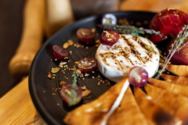 Izgara peyniri ile pişmiş elma ve üzüm ile dilim ekmek, rustik tarzı ahşap arka plan üzerinde siyah bir tabakta servis. Restoran hizmet