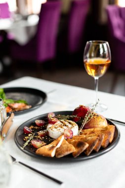 Izgara peyniri ile pişmiş elma ve üzüm ekmek tortilla, dilimleri ile servis beyaz masa örtüsü, aletleri ve bir kadeh şarap bir restoranda bir masada siyah bir plaka üzerinde