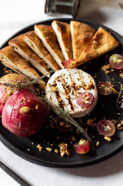 Izgara peyniri ile pişmiş elma ve üzüm ekmek tortilla, dilimleri ile servis beyaz masa örtüsü, aletleri ve bir kadeh şarap bir restoranda bir masada siyah bir plaka üzerinde