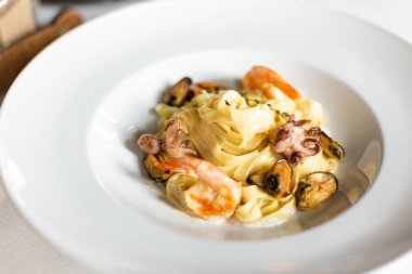 Deniz ürünleri kraft Yapıştır: midye, karides ve ahtapot bir kremalı sos servis beyaz masa örtüsü, aletleri ve bir kadeh şarap bir restoranda bir masada beyaz tabakta