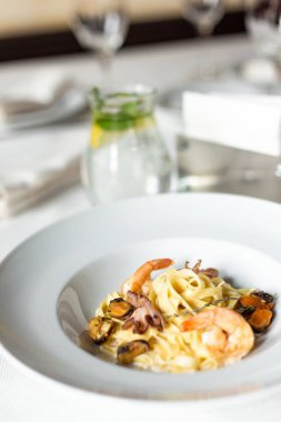 Deniz ürünleri kraft Yapıştır: midye, karides ve ahtapot bir kremalı sos servis beyaz masa örtüsü, aletleri ve bir kadeh şarap bir restoranda bir masada beyaz tabakta