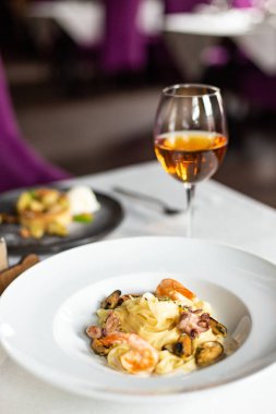 Deniz ürünleri kraft Yapıştır: midye, karides ve ahtapot bir kremalı sos servis beyaz masa örtüsü, aletleri ve bir kadeh şarap bir restoranda bir masada beyaz tabakta