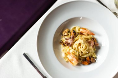 Deniz ürünleri kraft Yapıştır: midye, karides ve ahtapot bir kremalı sos servis beyaz masa örtüsü, aletleri ve bir kadeh şarap bir restoranda bir masada beyaz tabakta