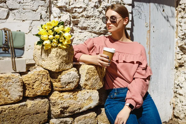 한 소녀가 커피 한 잔을 들고 도시 벽 근처에 서 있습니다. — 스톡 사진