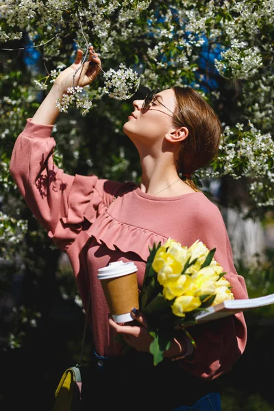 Chica en gafas de sol y gafas de suéter rosa con entre el árbol floreciente — Foto de Stock