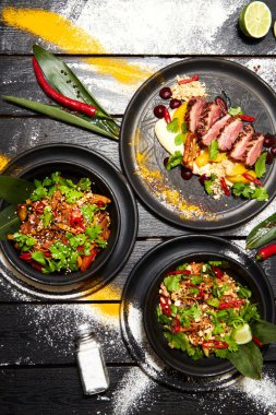 Siyah bir masada Asya yemekleri. Şeftali ile Ördek göğsü, sığır eti ile erişte, tavuk ve karides ile pad tay.