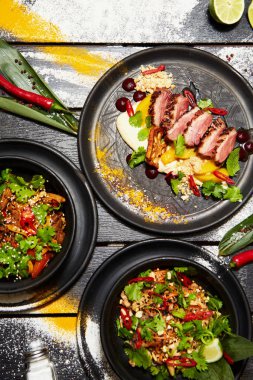 Siyah bir masada Asya yemekleri. Şeftali ile Ördek göğsü, sığır eti ile erişte, tavuk ve karides ile pad tay.