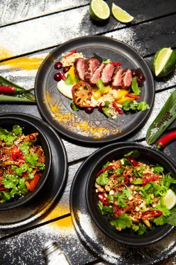 Siyah bir masada Asya yemekleri. Şeftali ile Ördek göğsü, sığır eti ile erişte, tavuk ve karides ile pad tay.