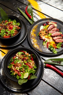 Siyah bir masada Asya yemekleri. Şeftali ile Ördek göğsü, sığır eti ile erişte, tavuk ve karides ile pad tay.